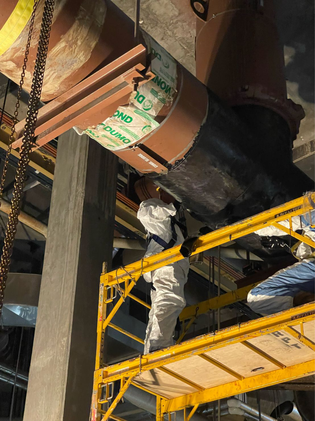 View looking up at workers repairing section of large pipeline.