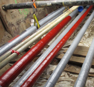 Multiple lines of pipe-type cables exposed exposed in the ground, some painted red and others gray.