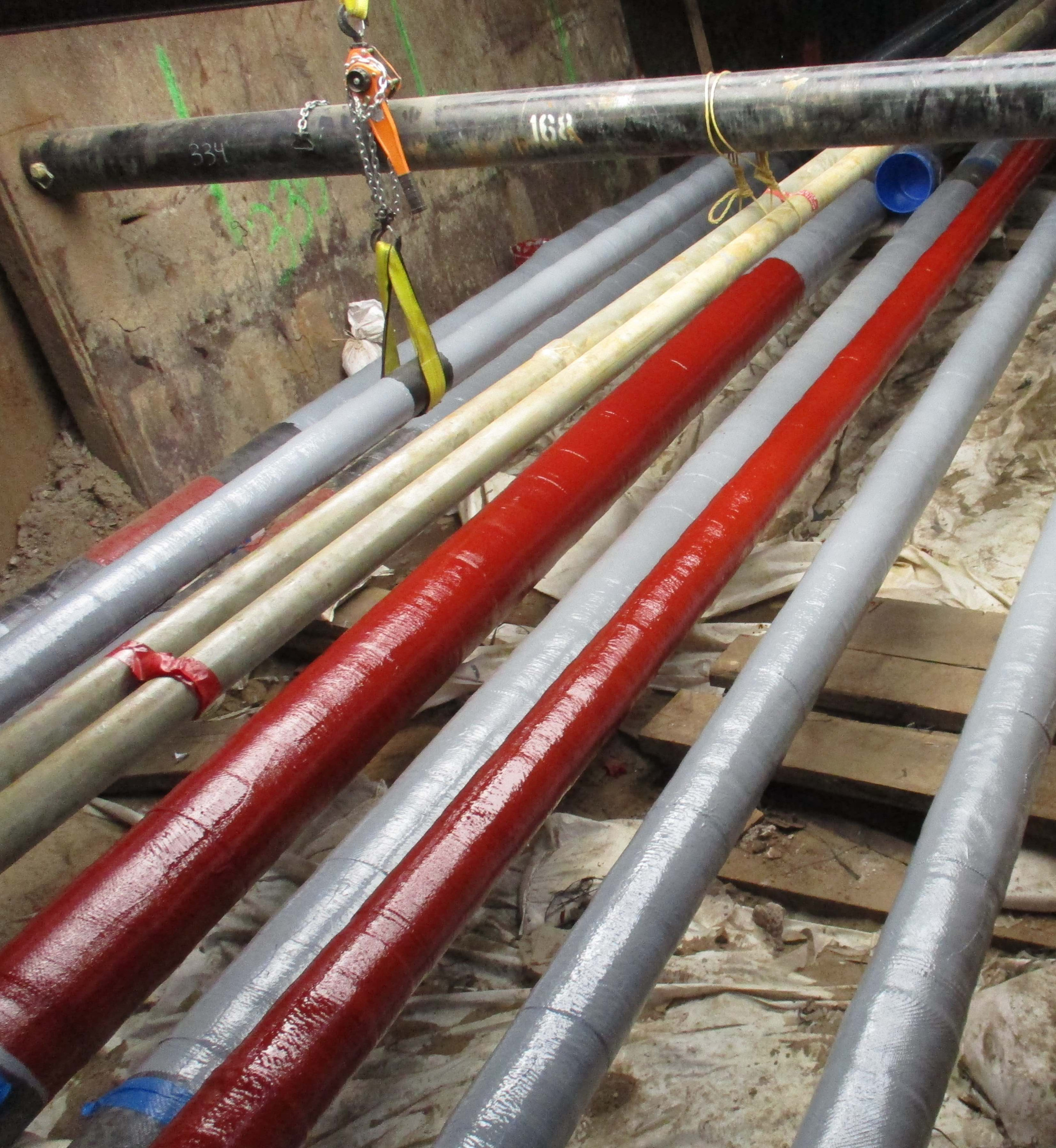 Multiple lines of pipe-type cables exposed exposed in the ground, some painted red and others gray.