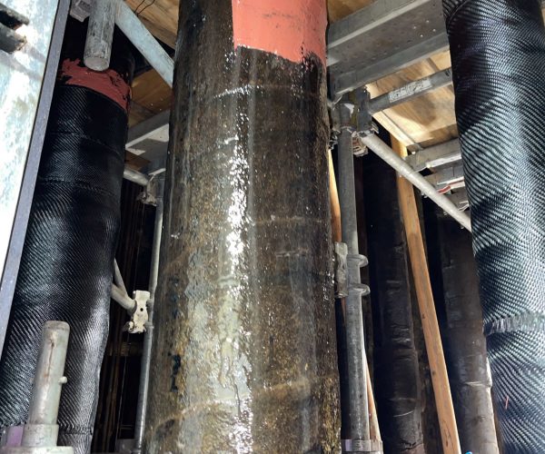 Three vertical pipes with composite pipe repair wrapped around them.