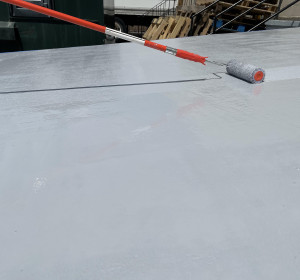 Roller applying gray coating to concrete loading ramp.