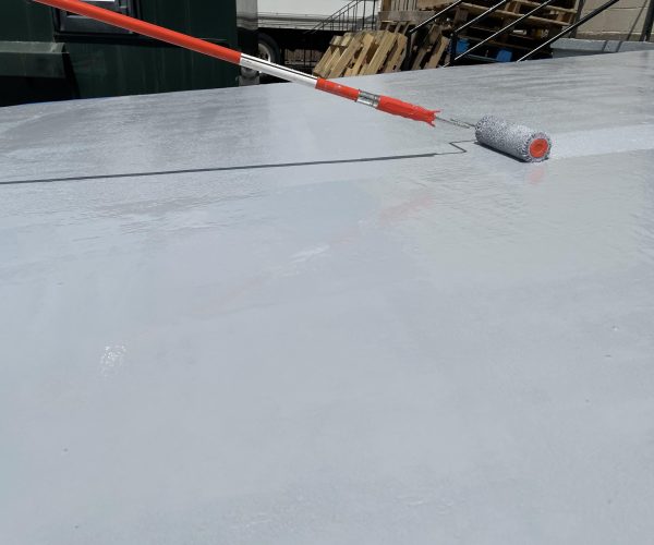 Roller applying gray coating to concrete loading ramp.