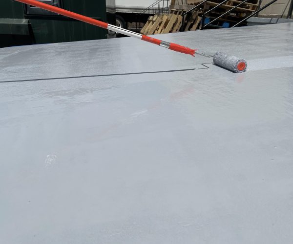 Roller applying gray coating to concrete loading ramp.