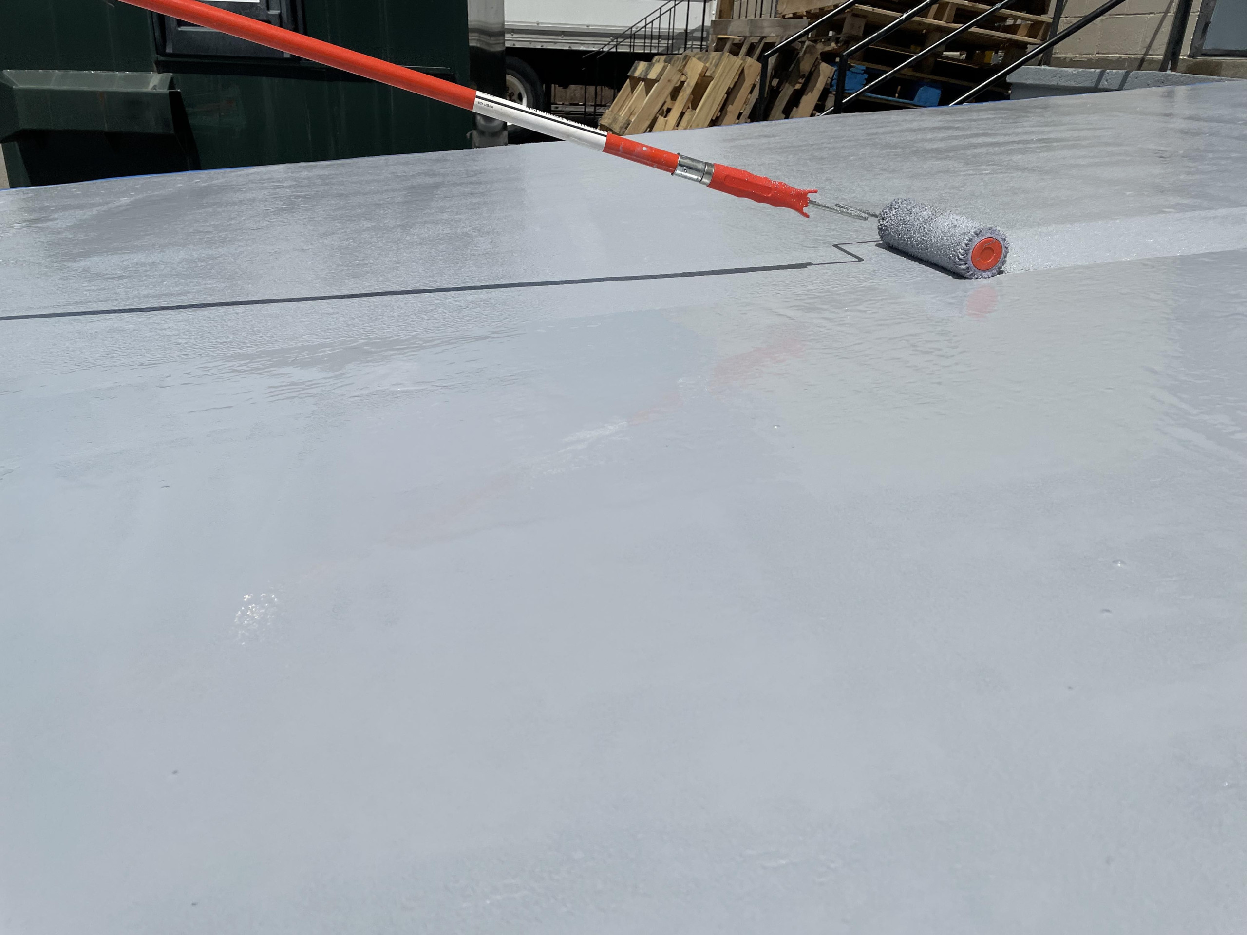 Roller applying gray coating to concrete loading ramp.