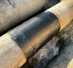 Composite pipe repair for waterwater treatment plant. Image of pipe wrapped in black composite wrap.