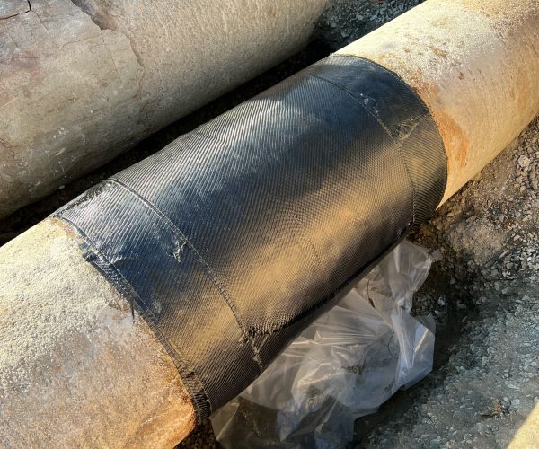 Composite pipe repair for waterwater treatment plant. Image of pipe wrapped in black composite wrap.