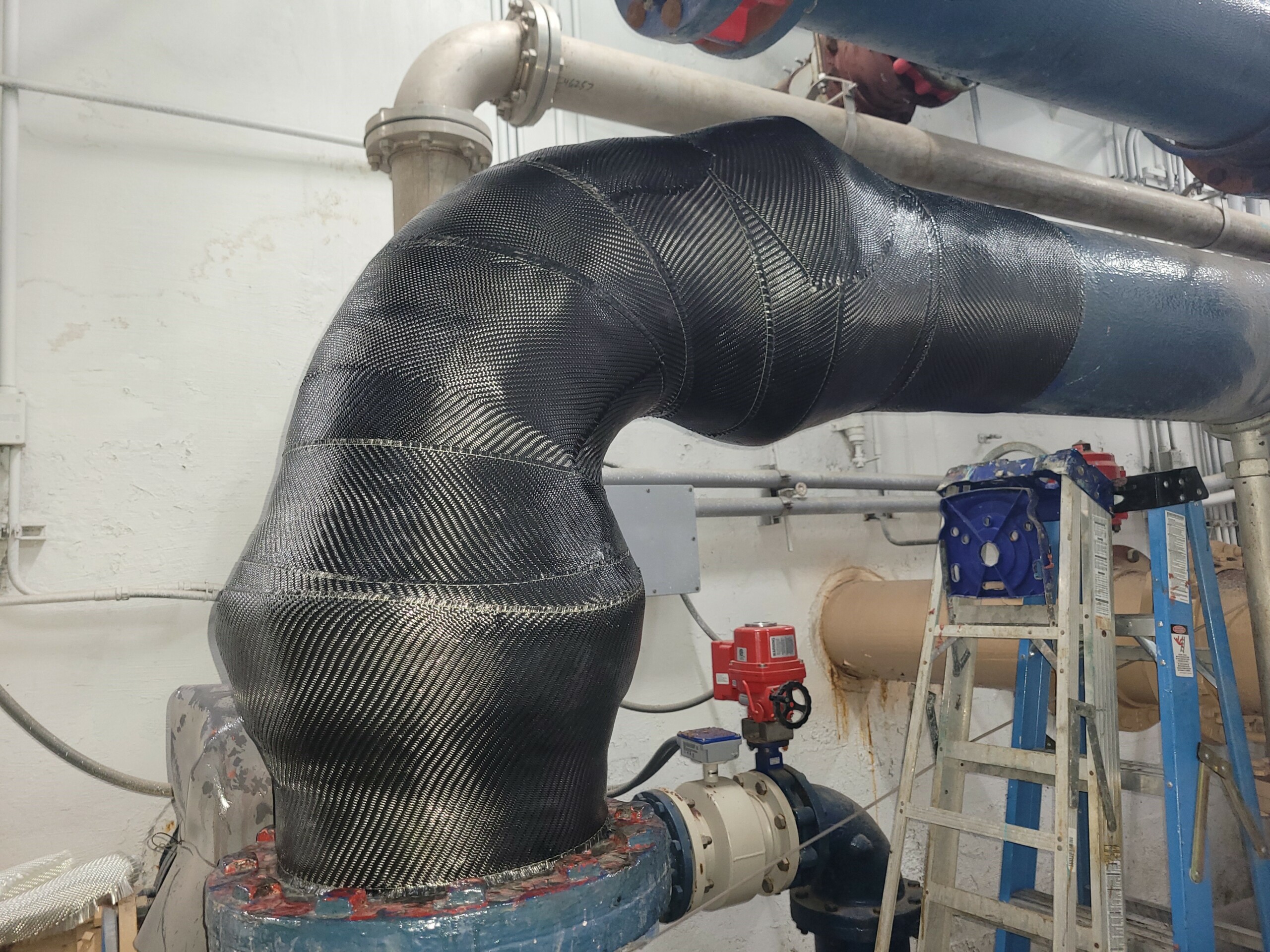 Large pipe elbow inside a water and wastewater facility wrapped in carbon fiber composite.