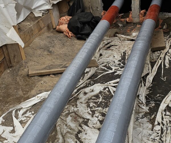 View of gray and red coated composite repair wrapped on a pipe in a trench