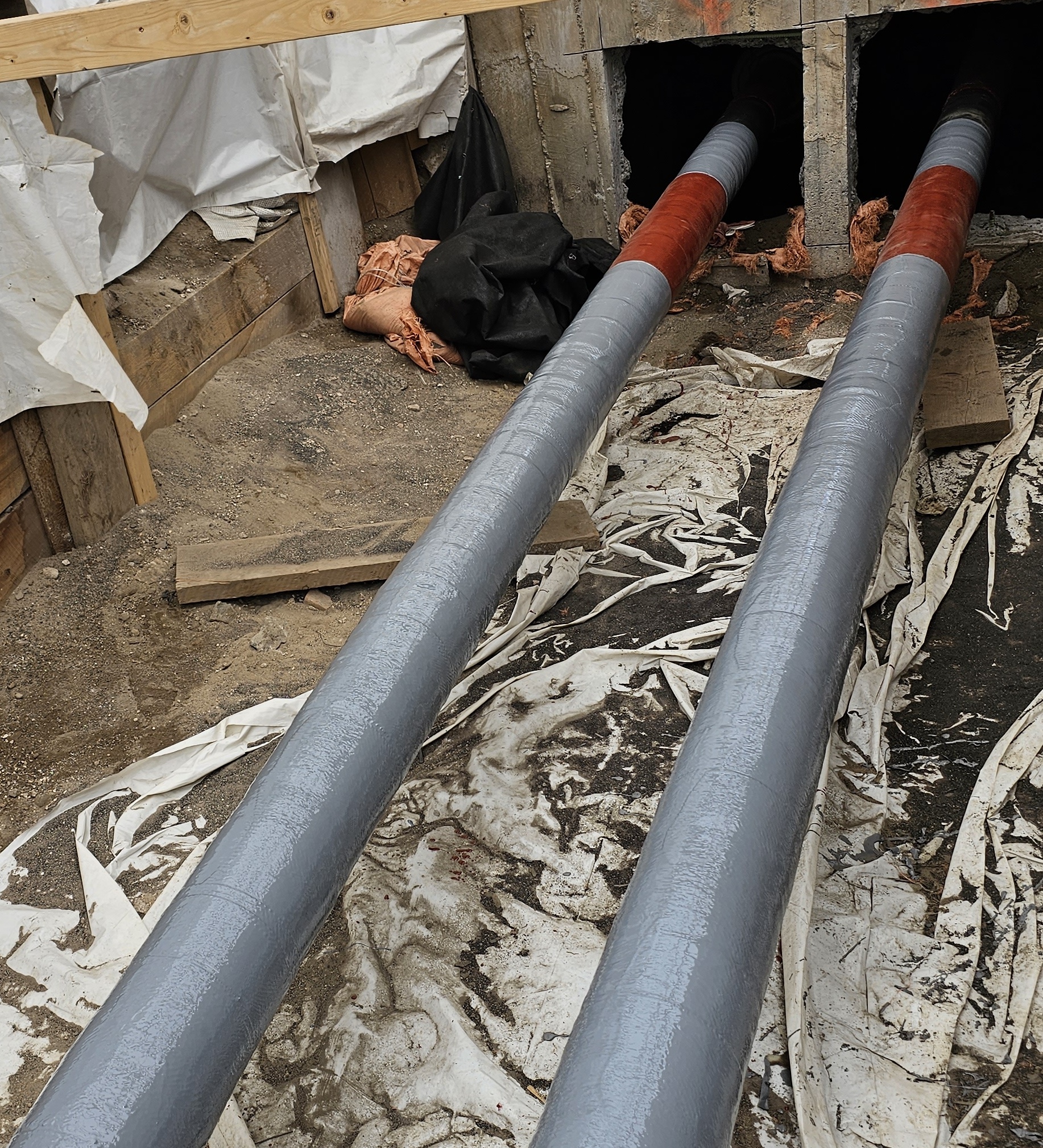 View of gray and red coated composite repair wrapped on a pipe in a trench