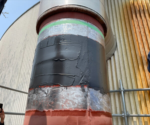 Large diameter vertical pipe outside facility wrapped around the width with carbon fiber composite repair material.