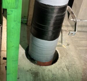 Large pipe wrapped at the base with a black fabric carbon fiber composite repair