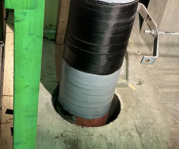 Large pipe wrapped at the base with a black fabric carbon fiber composite repair