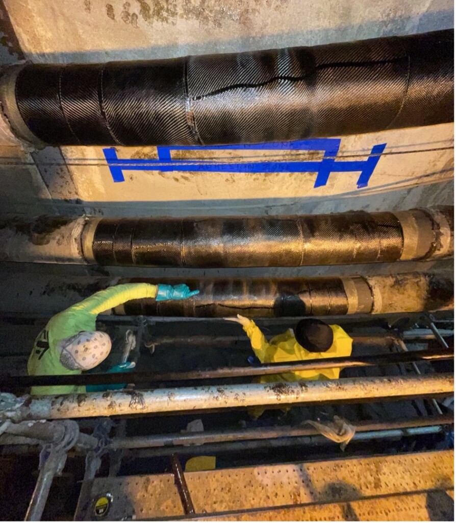 View of workers applying composite pipe repairs in an excavated trench surrounded by power transmission pipe-type cables